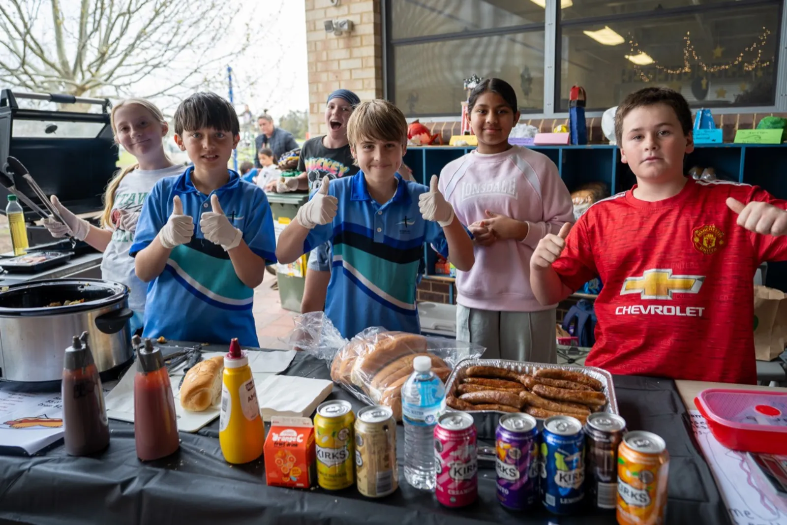 Bunbury Baptist College Primary students giving a thumbs up at a sausage sizzle fundraiser